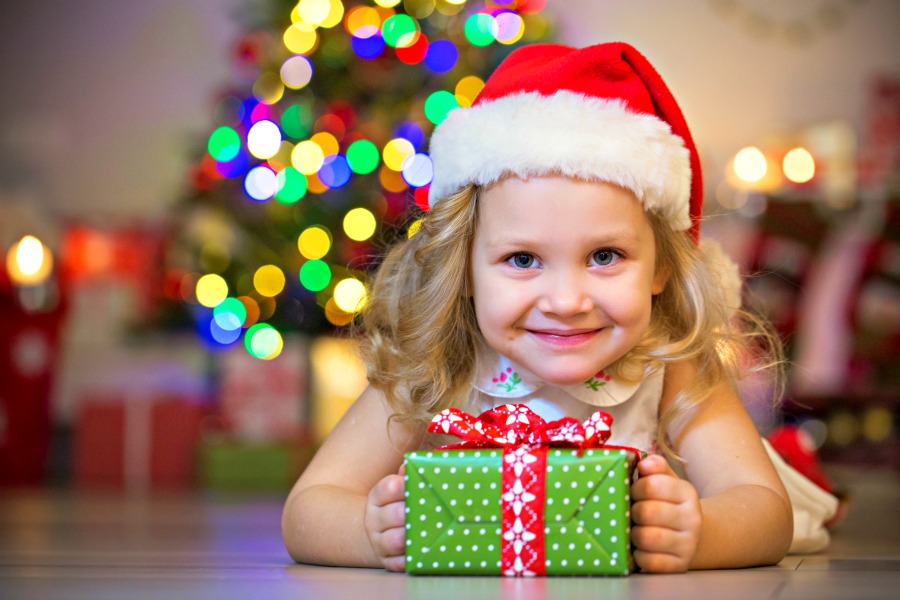Girl in Santa hat with gift. Good holiday safety practice to check the age ranges of toys before gifting.